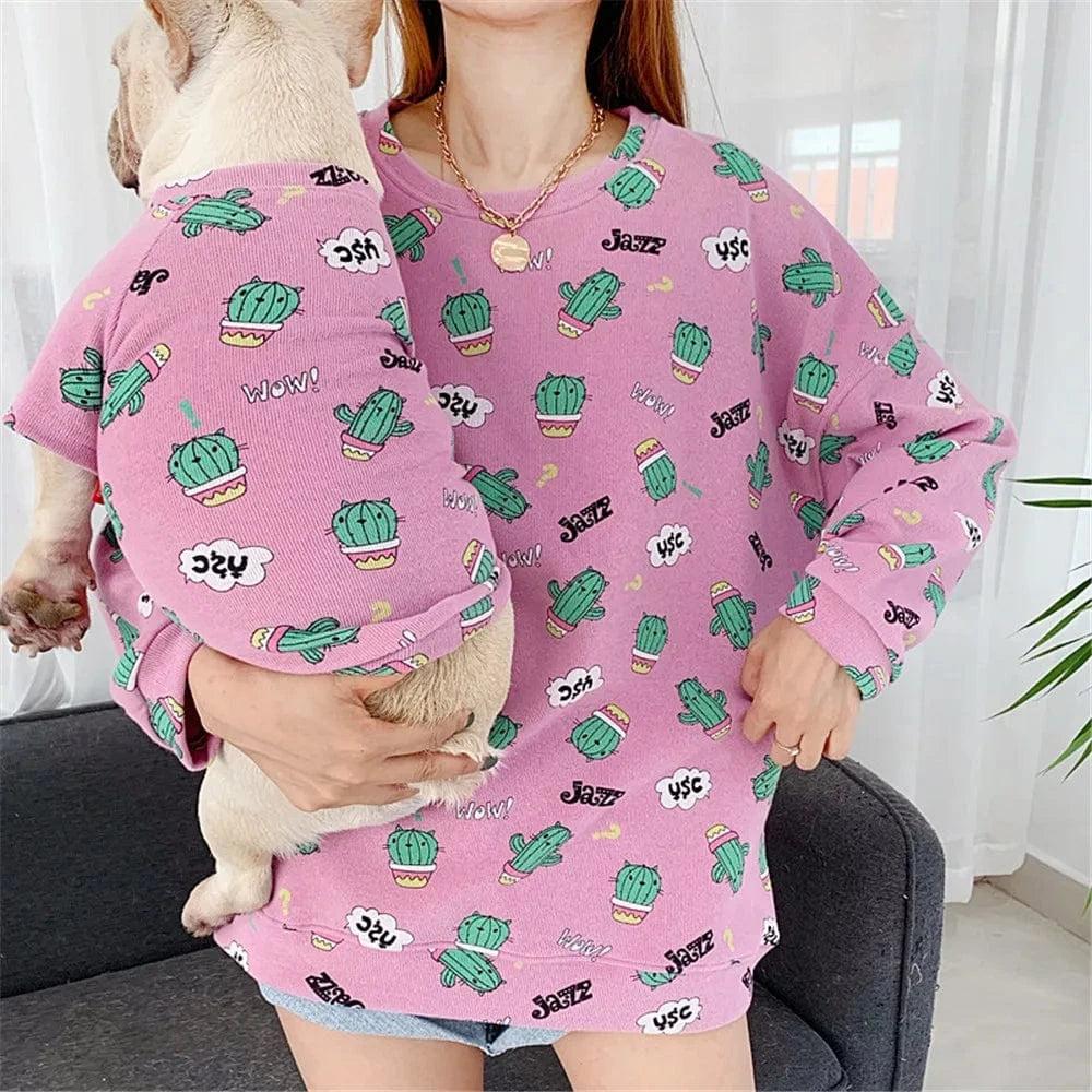 A person holds a dog, both wearing matching pink fabric sweatshirts with a green cactus pattern and Jazz and WOW! text.