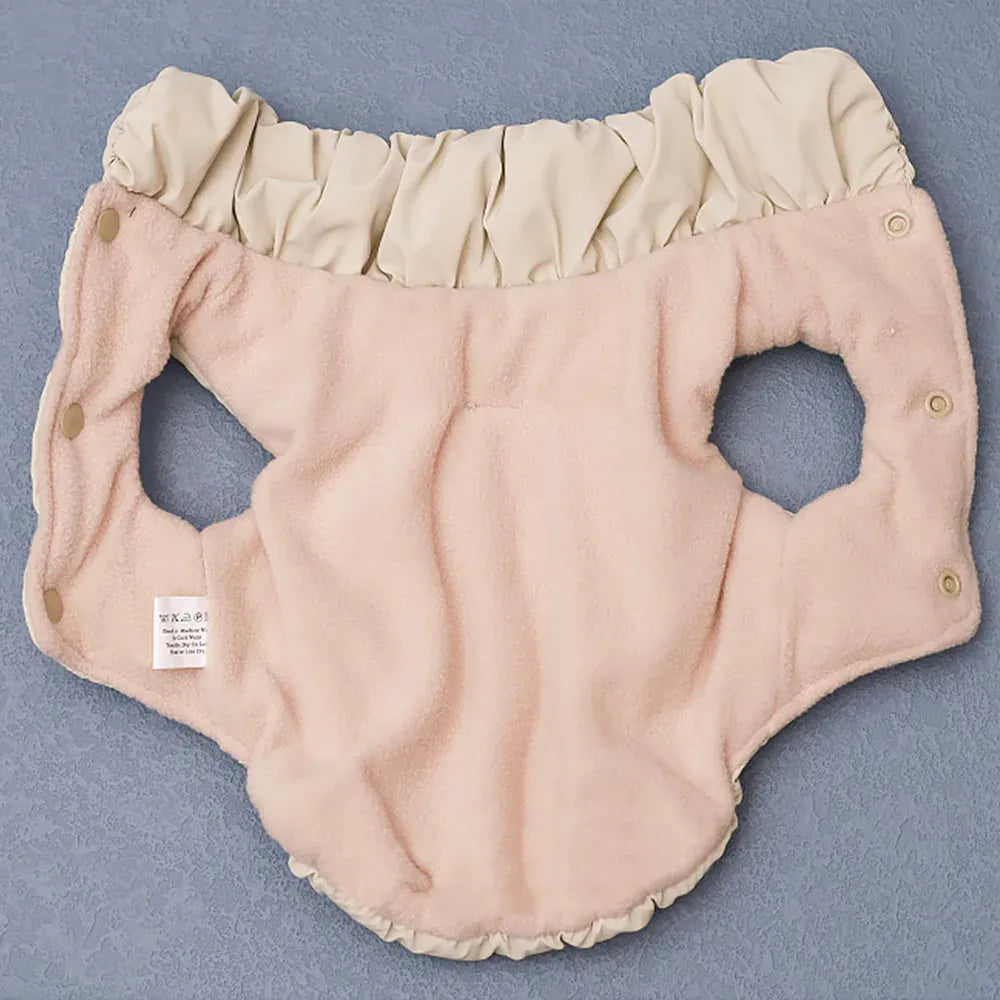 Pink fleece-lined dog coat with a tan ruffled collar and snap buttons, laid flat on a blue surface.