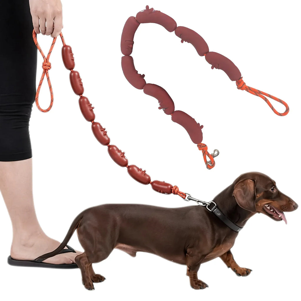 A brown dachshund wearing a black collar is shown walking on an orange leash made of sausage-shaped brown pads, with a person's leg and hand visible holding the leash on a white background.
