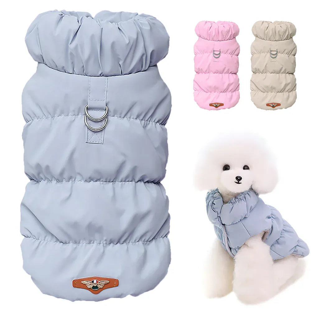 Three padded fabric dog coats in blue, pink, and beige with metal D-rings, shown flat and worn by a small white dog.