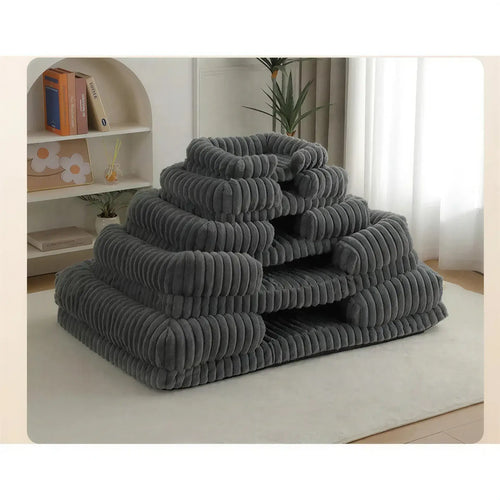 Four grey ribbed fabric dog beds in various sizes stacked in a pyramid on a white rug.
