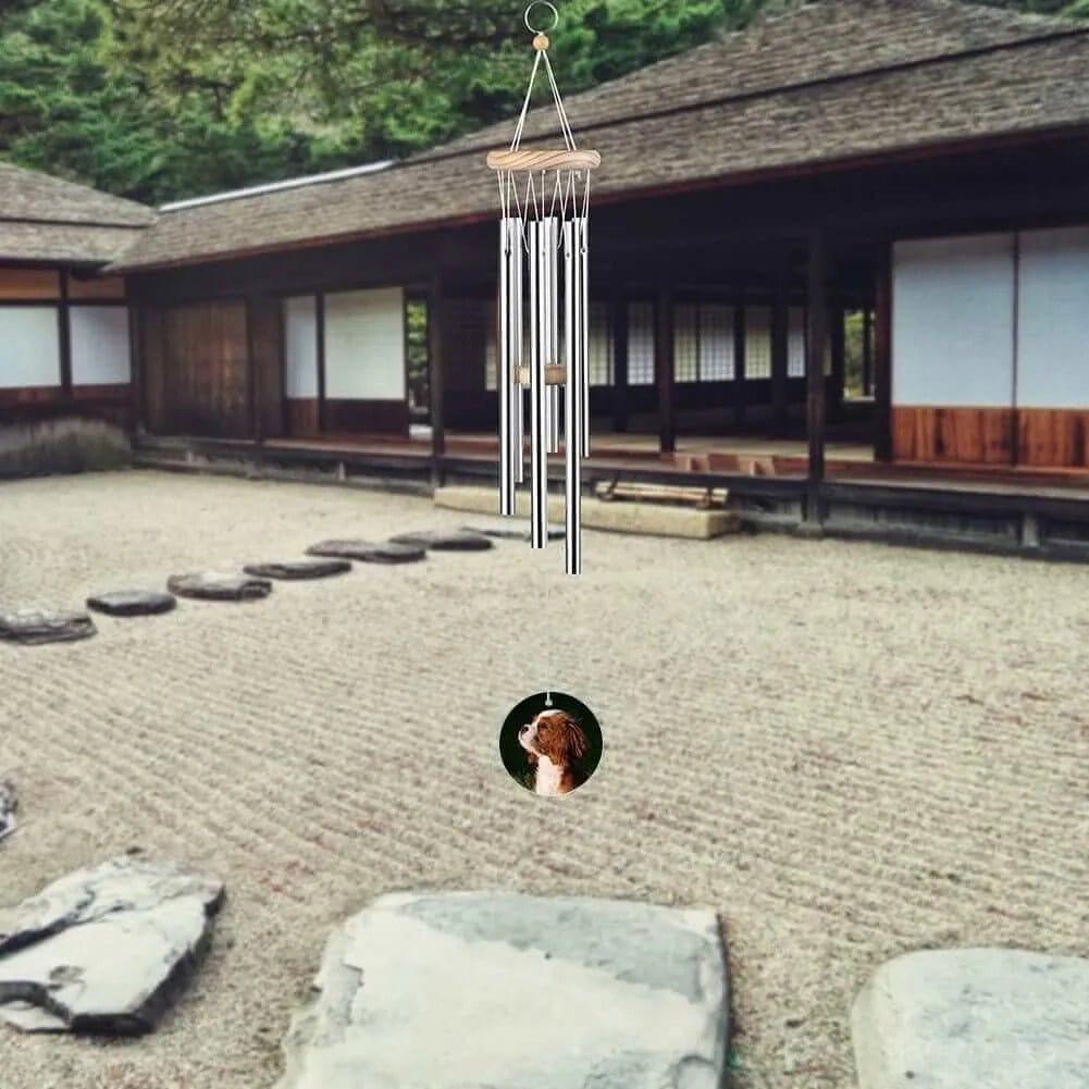 Silver metal wind chimes with wood accents and a round pendant featuring a dog, hanging over a zen rock garden.