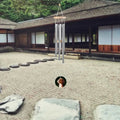 Silver metal wind chimes with wood accents and a round pendant featuring a dog, hanging over a zen rock garden.